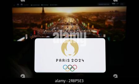 Person holding smartphone with logo of the 2024 Summer Olympics in Paris on screen in front of website. Focus on phone display. Stock Photo