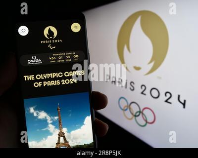 Person holding smartphone with website of the 2024 Summer Olympics in Paris on screen in front of logo. Focus on center of phone display. Stock Photo