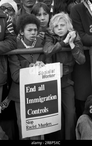 Black British boy and white friend  1970s UK United Against Racialism, a Labour Party and TUC rally and march to Trafalgar Square. Two friends, a black British and caucasian teenage boys carry a Socialist Workers party placard, 'End all Immigration Controls. Stop Racist Murders'. London, England 21st November 1976. HOMER SYKES Stock Photo