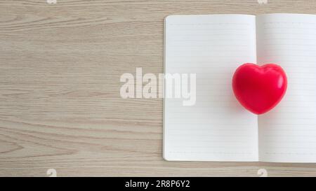 Top view of red heart love on an open and empty notebook on wooden background with copy space. Stock Photo