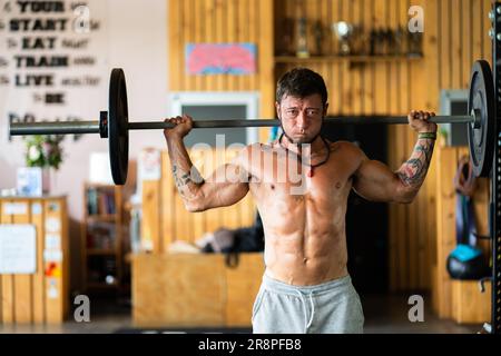 Man doing squats with weight using a bar in a gym Stock Photo