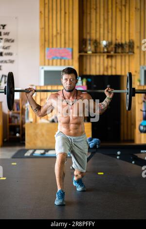 Fit man doing squats with weight using a bar in a gym Stock Photo