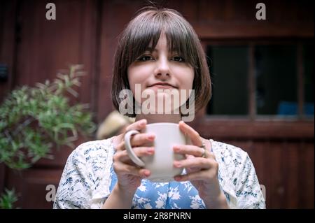 Happy teenage girl with cup drinking cocoa at city street cafe terrace. Drinks and people concept. Teenage girl drinking  in cafe Stock Photo