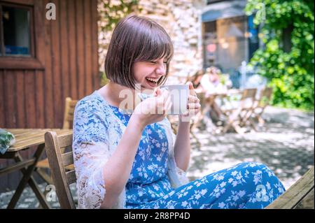 Happy teenage girl with cup drinking cocoa at city street cafe terrace. Drinks and people concept. Teenage girl drinking  in cafe Stock Photo