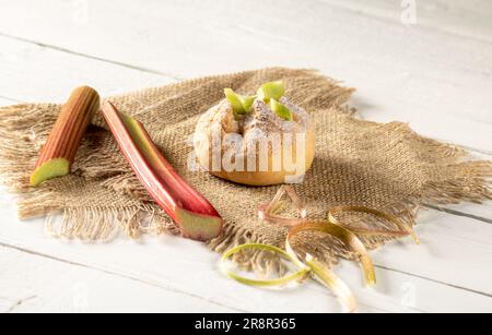 Rhubarb bun and rhubarb stalks on a burlap napkin on a wooden table. Stock Photo
