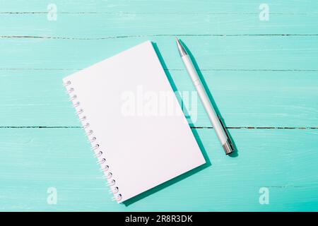 Notepad and pen on turquoise blue table in sunlight. Top view, flat lay, mockup. Stock Photo