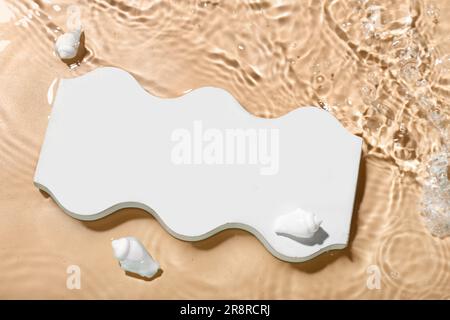 Plaster podium and seashells in water on beige background Stock Photo