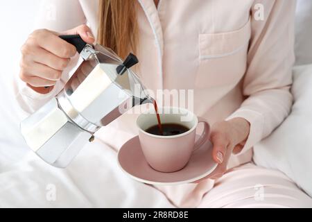 Woman pouring espresso from geyser coffee maker into cup in bed Stock Photo