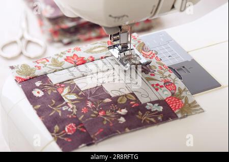 Patchwork log cabin blocks on electric sewing machine, stack of blocks, sewing accessories Stock Photo