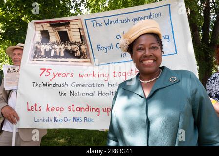 London, UK. 22 June, 2023. A woman in period clothes stands in front of a poster highlighting the contribution of immigrants from the Caribbean to the National Health Service at the start of the Windrush Procession  marking the 75th anniversary of the arrival at the Port of  Tilbury of the Empire Windrush. Credit: Ron Fassbender/Alamy Live News Stock Photo