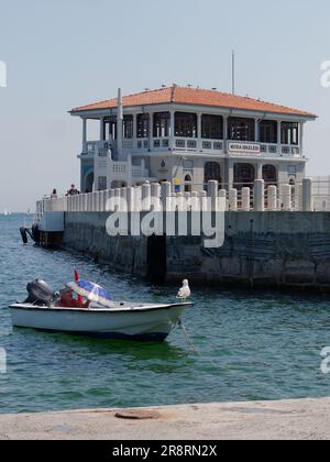 Man uses an umbrella for shade on his boat with a pier behind in the Kadikoy district of Istanbul, Turkey Stock Photo