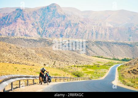 Fit young caucasian male person push bicycle uphill with mountains background outdoors in caucasus mountains. Achievement , inspiration, challenge and Stock Photo