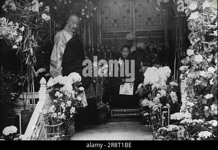 Tibet, Hermit Kingdom -- The 14th Dalai Lama sits on his throne in the Jewel Park (Norbhu-Lingka), surrounded by flowers. With him is one of his advisers. May 5, 1948. (Photo by Pictorial Press). Stock Photo