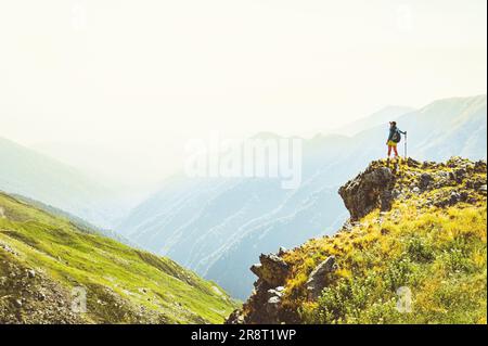 Back view fit sporty female hiker with nordic walk sticks stand on viewpoint uphill in green hiking trail in caucasus mountains .Recreational activiti Stock Photo