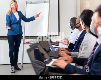 Female entrepreneurs in protective mask giving presentation to partners Stock Photo