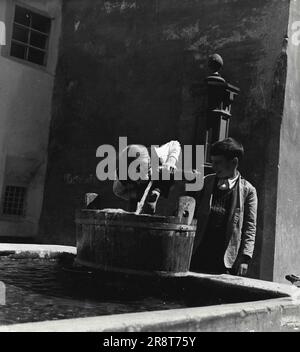 Pontresina -- Life in the High Alps of Switzerland. Boys Drink Clear Cold Water At The Well : All over Pontresina there are fountain-like wells with constantly running fresh water. Women do their washing here, children and adults often stop for a cool refreshing drink. Water comes from the mountain brooks. January 22, 1948. (Photo by Pictorial Press). Stock Photo