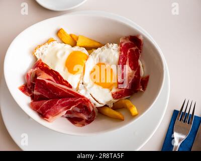 Fried eggs with fried potatoes and sliced cured ham Stock Photo