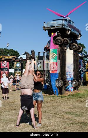 Glastonbury, UK. 22nd June, 2023. Festival goers perform hand-stands to emulate Joe Rush's 'Carhenge'. Carhenge revisits an idea that originated at the 1987 festival, made of 24 iconic vintage cars erected in the centre of the festival to emulate the ancient stone structure. photographed during the Glastonbury Festival 2023 at the Worthy Farm. Picture by Julie Edwards Credit: JEP Celebrity Photos/Alamy Live News Stock Photo