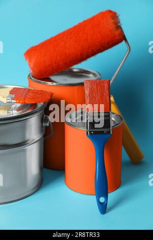 Cans of orange paint, bucket, roller and brushes on turquoise background Stock Photo