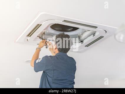 Worker repairing ceiling air conditioning unit in office. Stock Photo