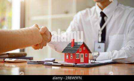 Close-up image of a professional male real estate agent or realtor shaking hands with a female client at a table in the office. property investment an Stock Photo