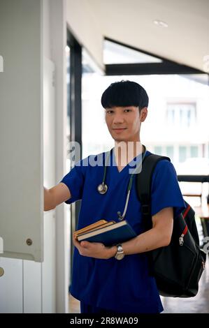 A handsome and happy young Asian male medical student or doctor in scrubs takes his belongings into a locker in the locker room at the medical college Stock Photo