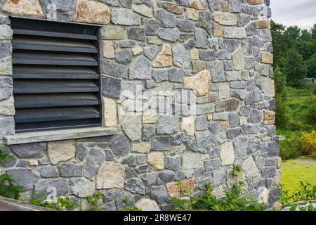 Window of a house closed with black wooden shutters. Old, ancient wood window with blind or shutters. Stone home facade. Old wooden slat shutter windo Stock Photo