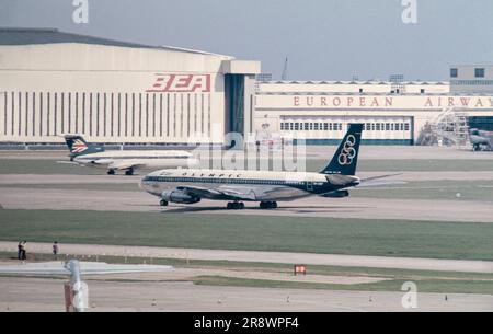 A 1974 photograph of aircraft at London Heathrow Airport. An Olympic Airways Boeing 707 and a BEA Trident are in the image, as well as the BEA Hangar. Stock Photo