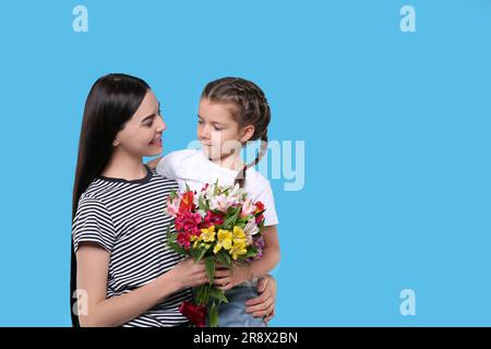 Happy woman with her daughter and bouquet of beautiful flowers on light blue background, space for text. Mother's day celebration Stock Photo