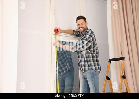 Man measuring window with tape indoors. Roller blinds installation Stock Photo