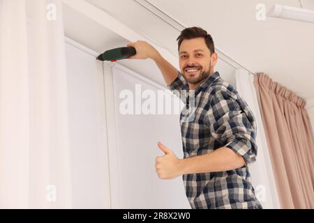 Man with drill installing roller window blind indoors Stock Photo