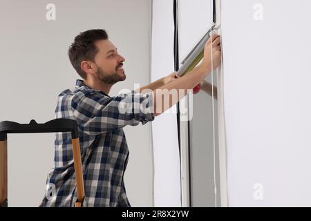 Man measuring window with tape on stepladder indoors. Roller blinds installation Stock Photo