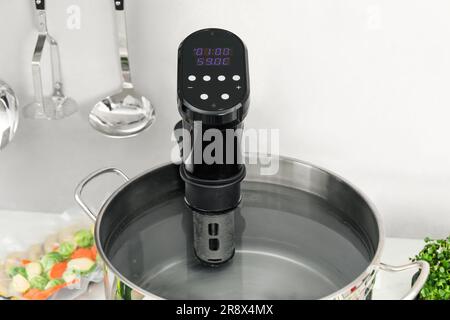 Sous vide cooker in pot on white table, closeup. Thermal immersion circulator Stock Photo