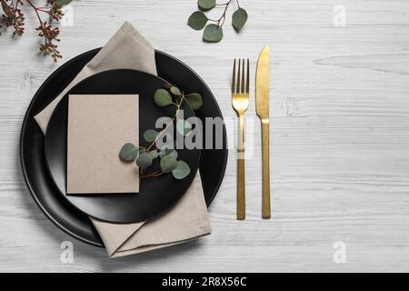 Stylish table setting with cutlery, blank card and eucalyptus leaves, flat lay. Space for text Stock Photo
