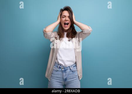 young dark-haired lady in informal clothes screaming on a blue background Stock Photo