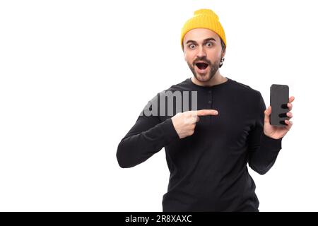 young surprised handsome caucasian brunette man with beard in informal style holding phone with mockup Stock Photo