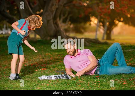 Father and son playing chess lying on grass at lawn park. Fathers Day Stock Photo
