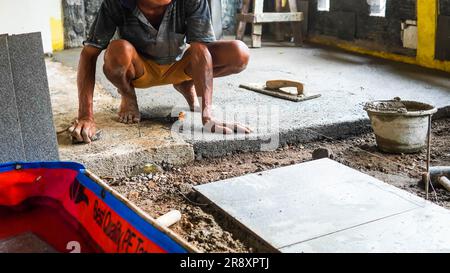 A male construction worker installs a large ceramic tile Stock Photo
