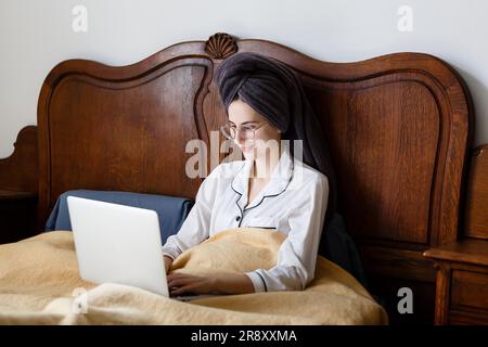 young woman with laptop in bed starts her day Stock Photo