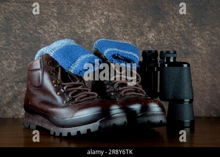 Hiking boots with binoculars and hiking socks on a polished wooden surface Stock Photo