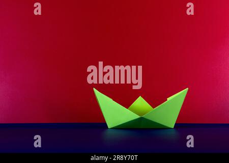 Yellow paper origami boat on a blue base and red background Stock Photo