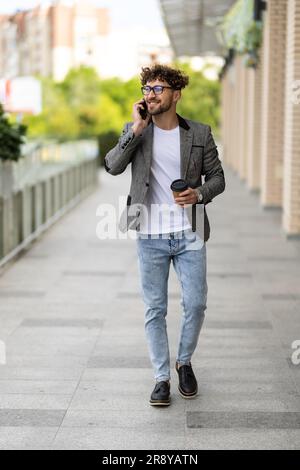 Young handsome man using smart phone with cup of coffee. Businessman holding mobile smartphone using app texting sms message wearing shirt. Stock Photo