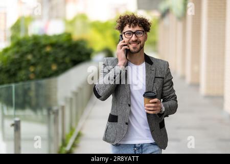Young handsome man using smart phone with cup of coffee. Businessman holding mobile smartphone using app texting sms message wearing shirt. Stock Photo