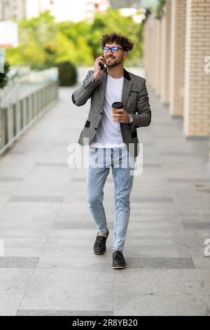 Portrait of handsome smiling man in casual wear holding smartphone. Successful manager makes a call. Young businessman talking on the phone, standing Stock Photo