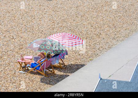 Lyme Regis, Dorset, UK. 23rd June, 2023. UK Weather: Sunseekers reading the newspaper on the beach at the seaside resort of Lyme Regis on an afternoon of hot sunshine . A hot and muggy start to the weekend with temperatures set to rise further over the weekend as the June heatwave continues into the weekend. Credit: Celia McMahon/Alamy Live News Stock Photo