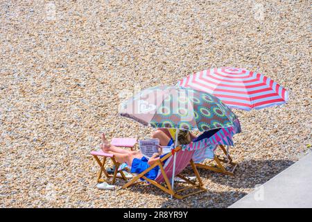 Lyme Regis, Dorset, UK. 23rd June, 2023. UK Weather: Sunseekers reading the newspaper on the beach at the seaside resort of Lyme Regis on an afternoon of hot sunshine . A hot and muggy start to the weekend with temperatures set to rise further over the weekend as the June heatwave continues into the weekend. Credit: Celia McMahon/Alamy Live News Stock Photo