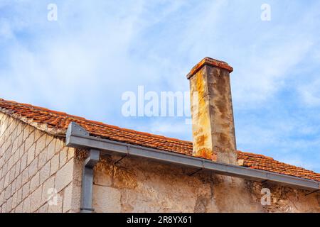 Old brick chimney on the roof of a house against the blue sky . Wall are made up of rectangular blocks Stock Photo