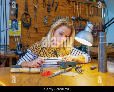 Netherlands, woman goldsmith in workshop designs and works on a bracelet in her studio. Stock Photo