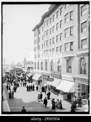 Young's Hotel and boardwalk, Atlantic City, N.J., c1904. Shops and drug stores selling: 'Shinn's orange juice, Caswell's salt water taffy, &quot;immense&quot; chewing candy, ice cream soda, Mexican penochis, hot chocolate, Ballardvale Lithia water, 10c cigar, tin types'. In the distance are the American Garden and Brady's Baths. People are being pushed in Bath chairs. Stock Photo