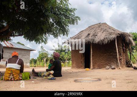 Old lady from Makonde tribe sitting in primitive kitchen and preparing local traditional meal. Simple metallic pot on fire between stones Stock Photo